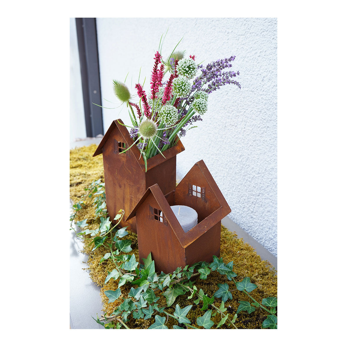 Zwei Leonos Haus zum Bepflanzen Edelrost Vasen mit Blumen auf moosigem Grund.