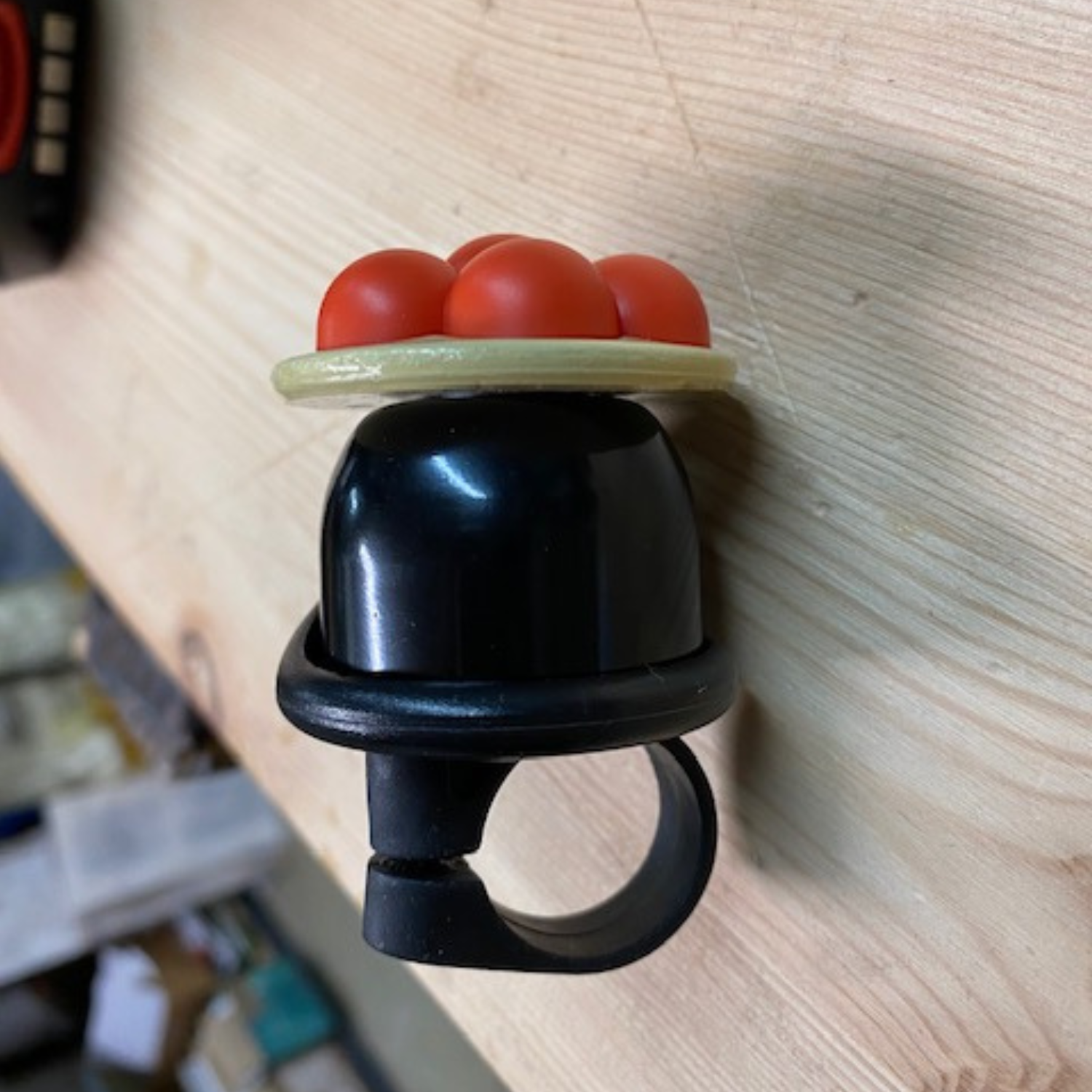 Die Schwarzwald Bollenhut Fahrradklingel mit schwarzem Kunststoffring, gelber Plattform und fünf roten Kugeln erinnert an den legendären Bollenhut-Stil. Sie verleiht jedem Fahrrad den Charme des Schwarzwalds und ist auf einer Holzoberfläche ein echter Hingucker.