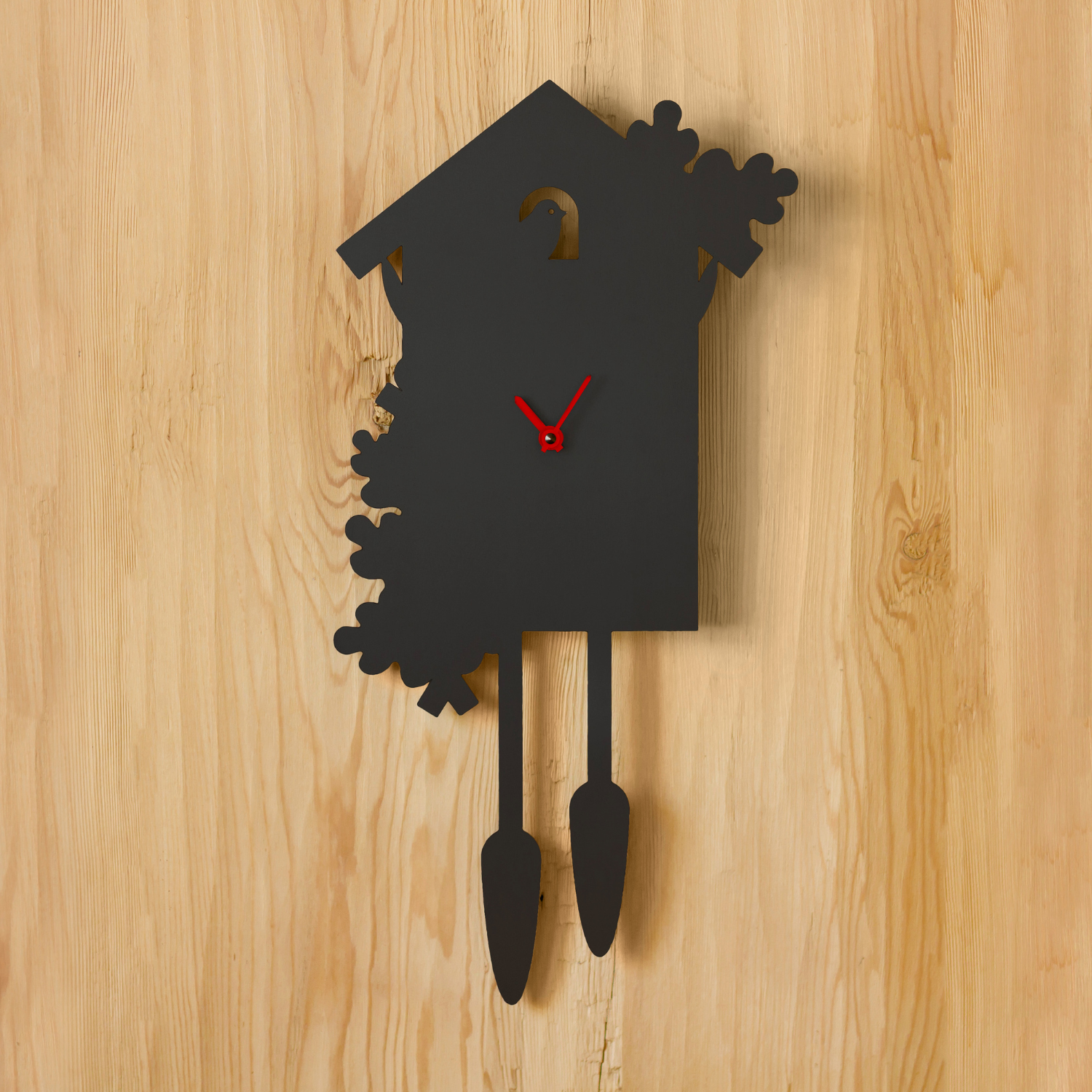 Die Wanduhr Jubi Kuckucksuhr mit modernem, zeitlosem Design und roten Zeigern hängt an einer hellen Holzwand.