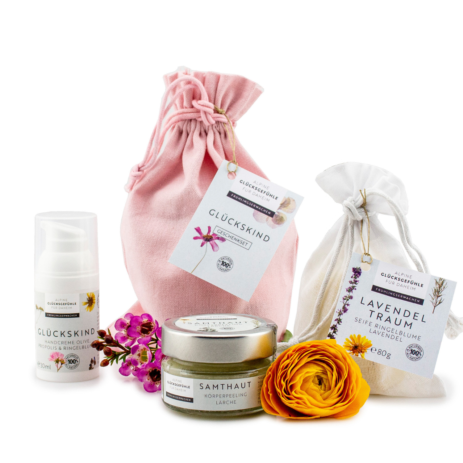 Das Geschenkset „Glückskind“ beinhaltet Handcreme Olive, Propolis Lavendeltraum Pflegeprodukte, Blumen und zwei Stoffbeutel mit deutscher Aufschrift, alles arrangiert auf weißem Hintergrund.