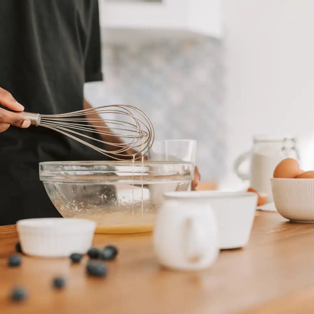 Person, die die Zutaten in einer Glasschüssel auf einer hölzernen Küchenarbeitsplatte verquirlt.