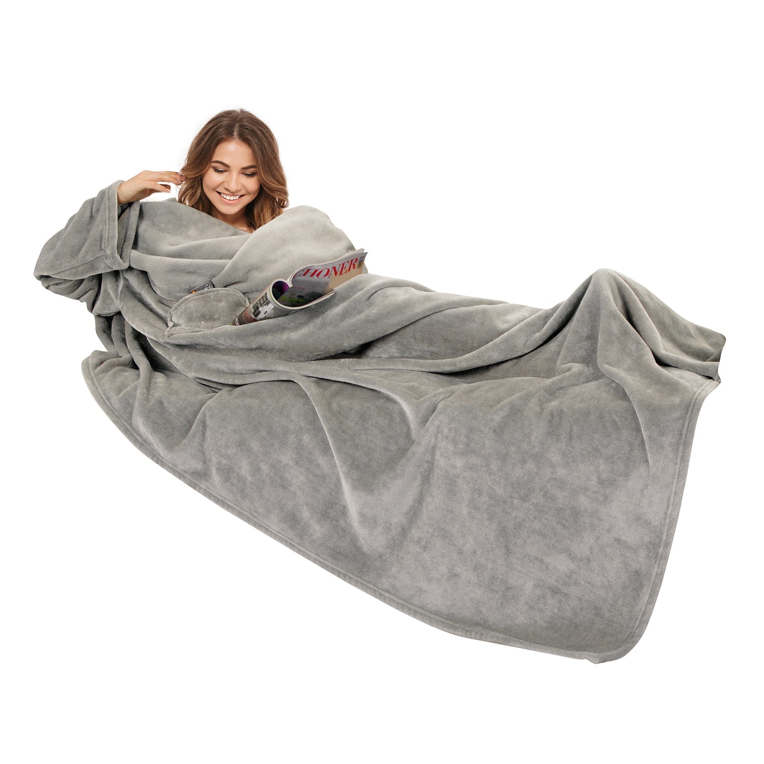 Eine Frau, eingehüllt in eine große graue Kuscheldecke mit Ärmeln, lehnt sich bequem zurück, lächelt und hält eine Zeitschrift in der Hand, was vor einem schlichten weißen Hintergrund eine gemütliche Atmosphäre suggeriert.