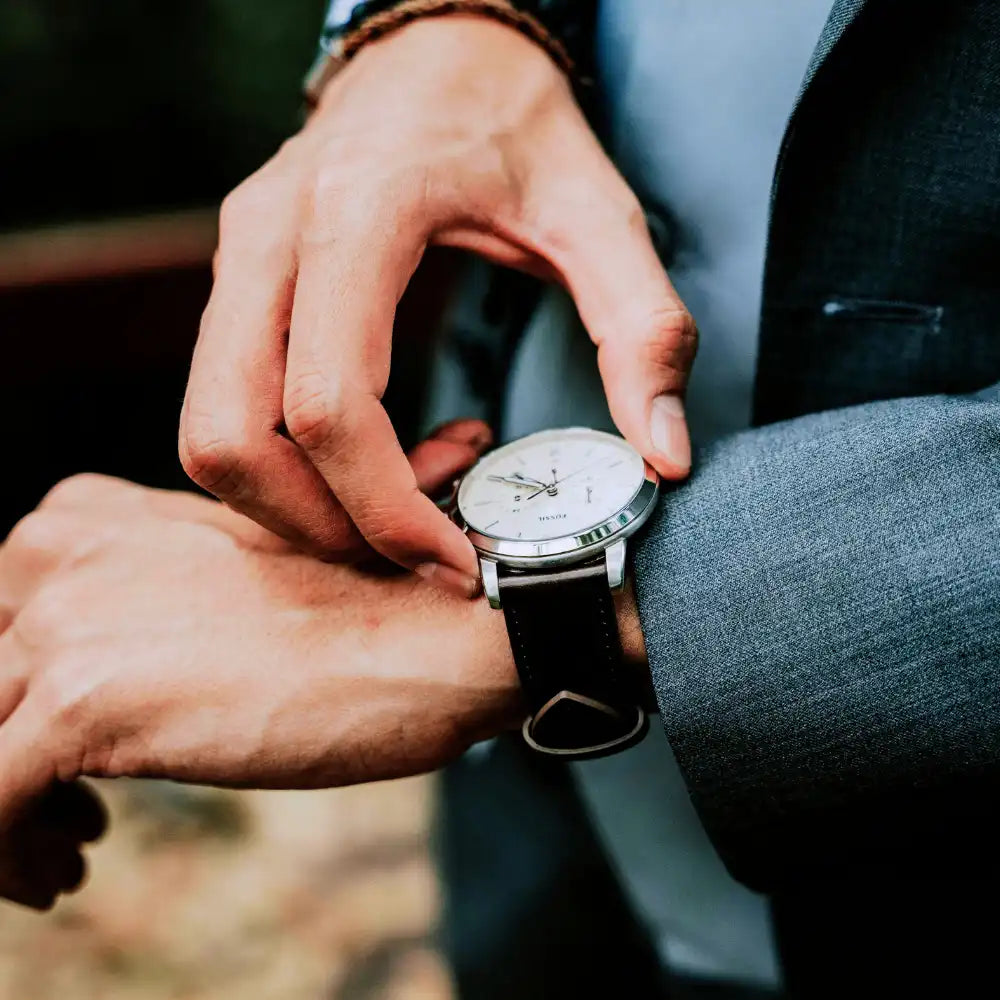 Person, die eine silberne Armbanduhr einstellt, während sie einen blauen Anzug trägt.