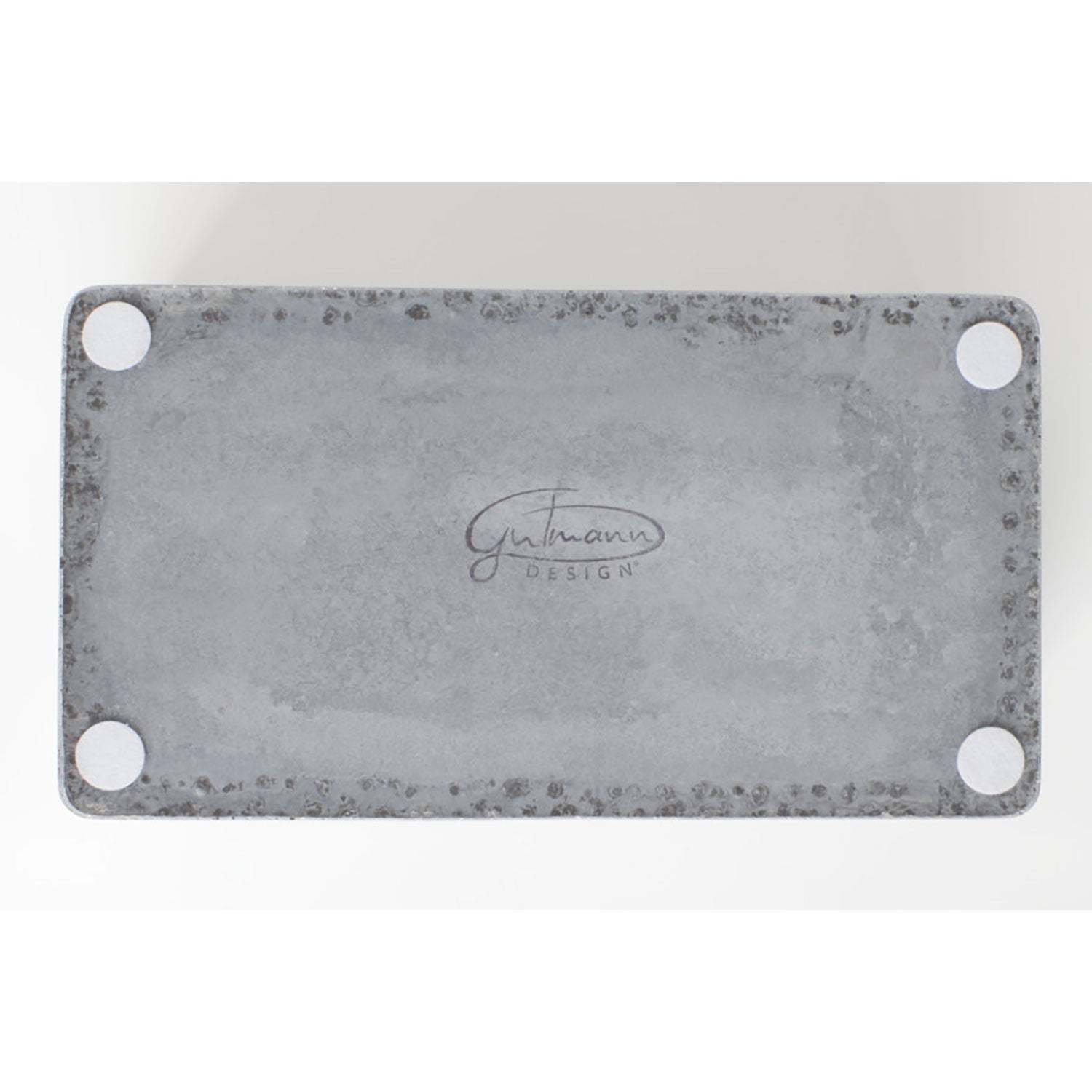 Der Brotkasten mit Eichenholzdeckel ist eine graue, rechteckige Metallplatte mit vier runden Ecken und dem Schriftzug „Gutmann Design“ in der Mitte. Die verwitterte, strukturierte Betonoberfläche verströmt industriellen Charme.
