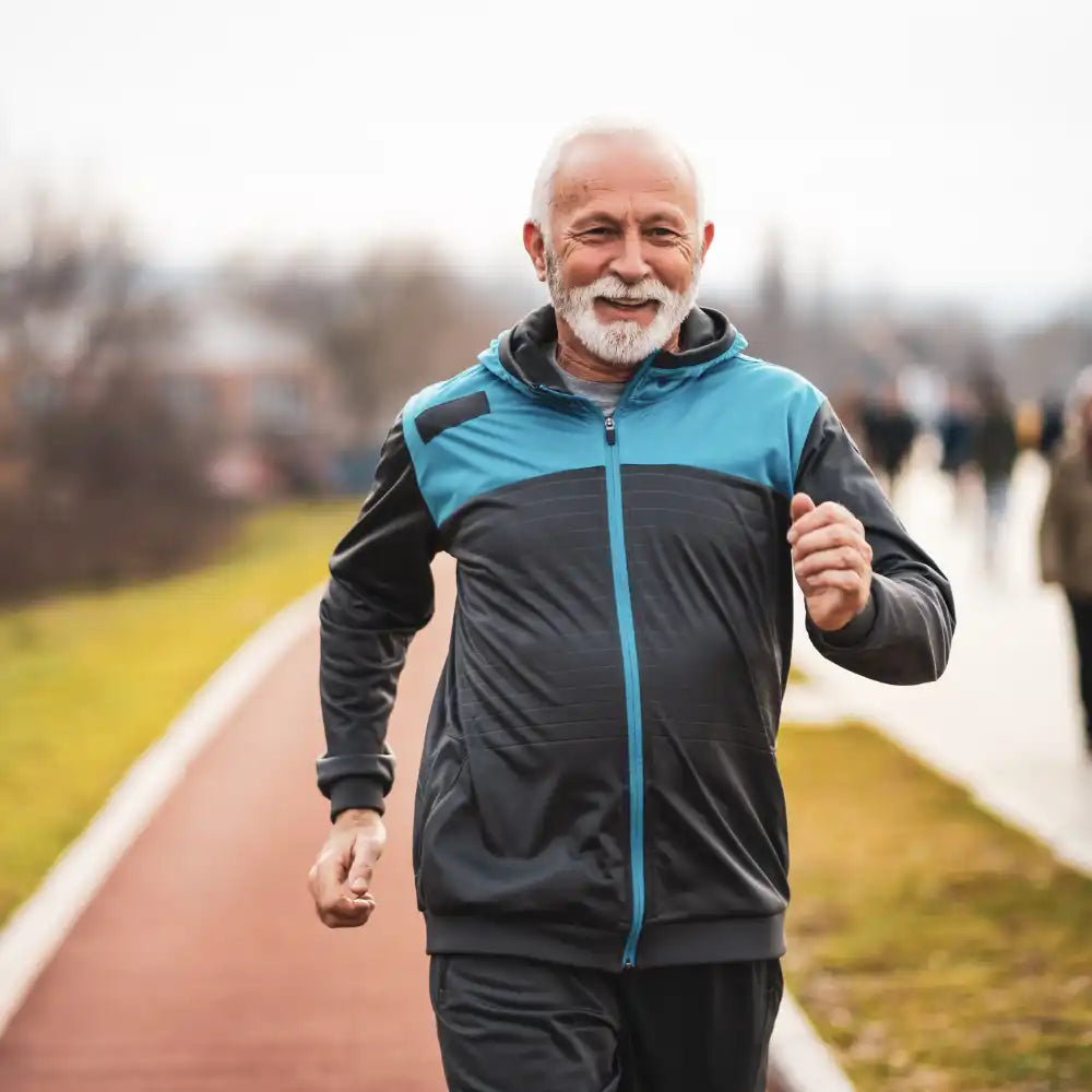 Älterer Mann joggt auf einem Parkweg, lächelt und trägt einen Trainingsanzug.