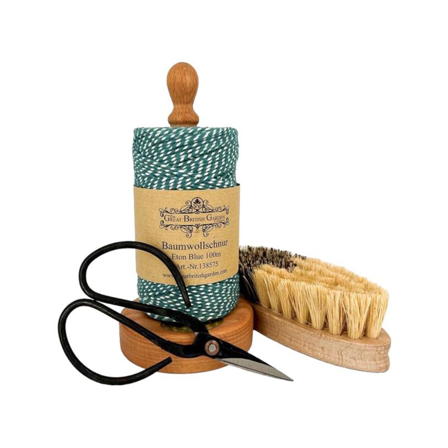 Das Geschenkset „Küchengarten“ mit grün-weißem Bäckergarn auf einem Holzhalter, einer schwarzen Vintage-Schere und einer kleinen Holzbürste mit hellen Borsten ist kunstvoll auf weißem Hintergrund arrangiert.