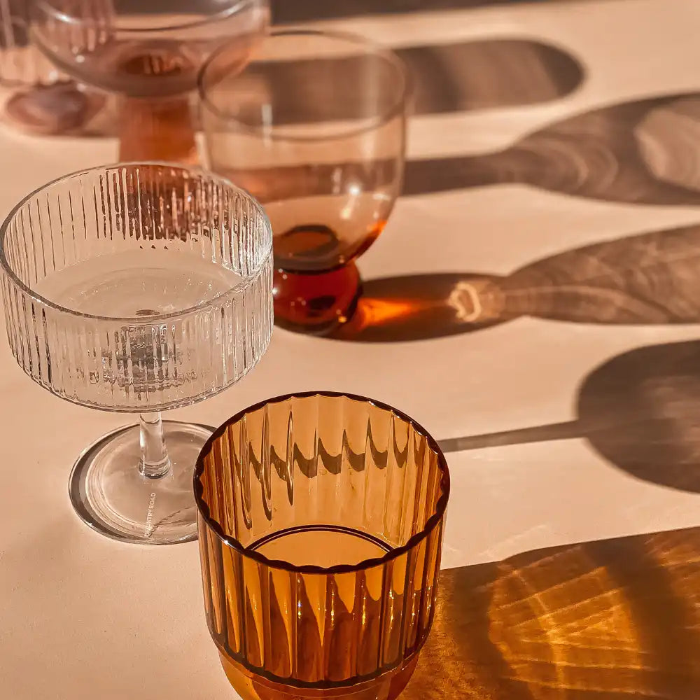 Gerippte Glasschalen werfen warme, langgestreckte Schatten auf eine beigefarbene Oberfläche.