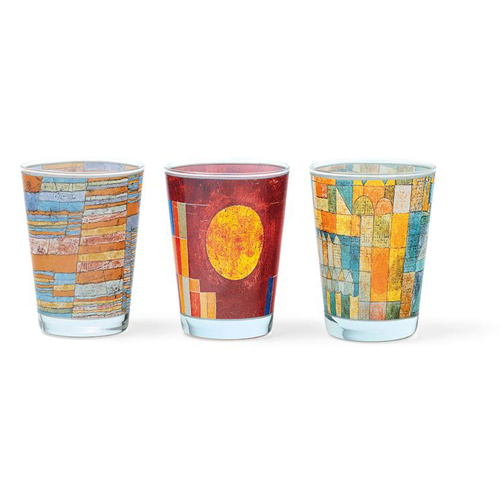 Die 3 Glas-Windlichter mit Künstlermotiven (Set 1) zeigen jeweils einzigartige, vom Bauhaus-Stil inspirierte Designs: eines mit blauen und orangefarbenen Streifen, ein anderes mit einer roten Sonne auf dunklem Hintergrund und das dritte mit einem geometrischen Muster in Grün und Orange, das an moderne Kunst erinnert.