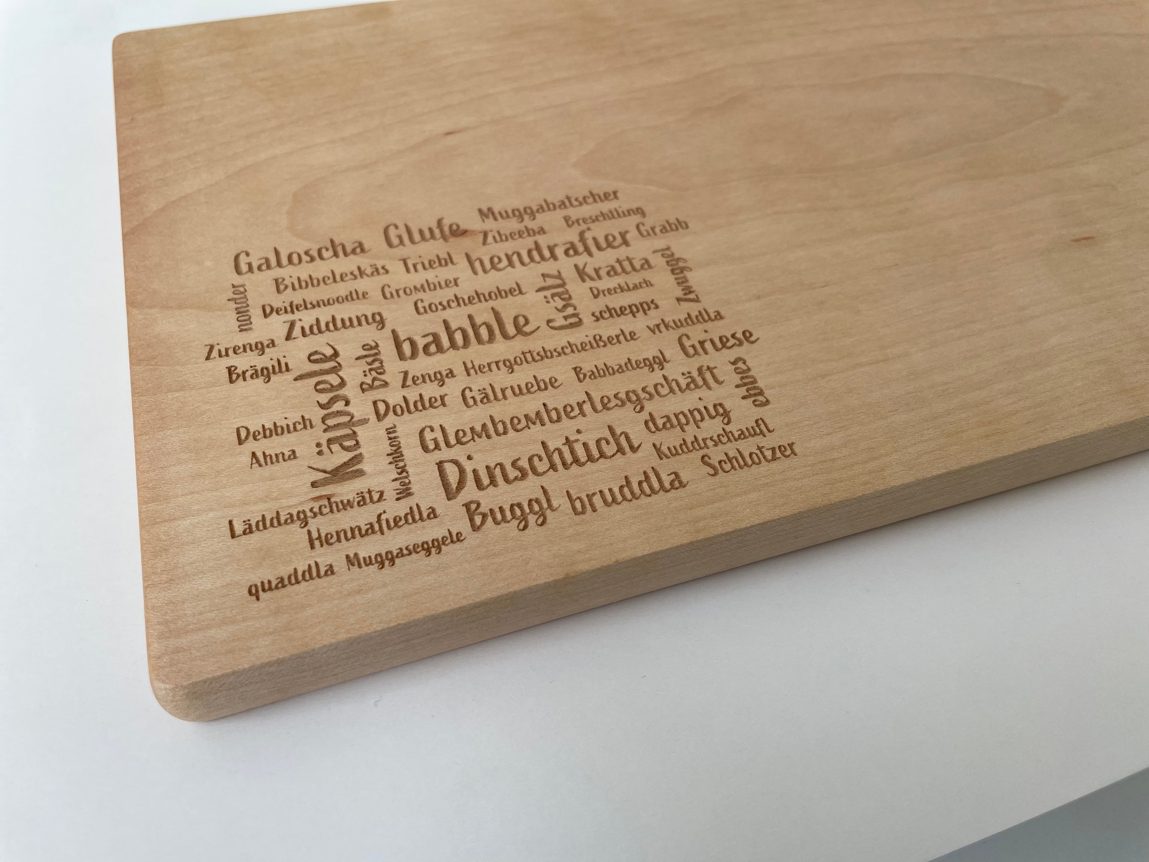 Das Mundart-Brettle ist ein graviertes Vesperbrett aus Holz, das mit deutschen Wörtern in unterschiedlichen Schriftarten und Größen verziert ist und die authentische Mundart-Gravur auf seiner Oberfläche hervorhebt.