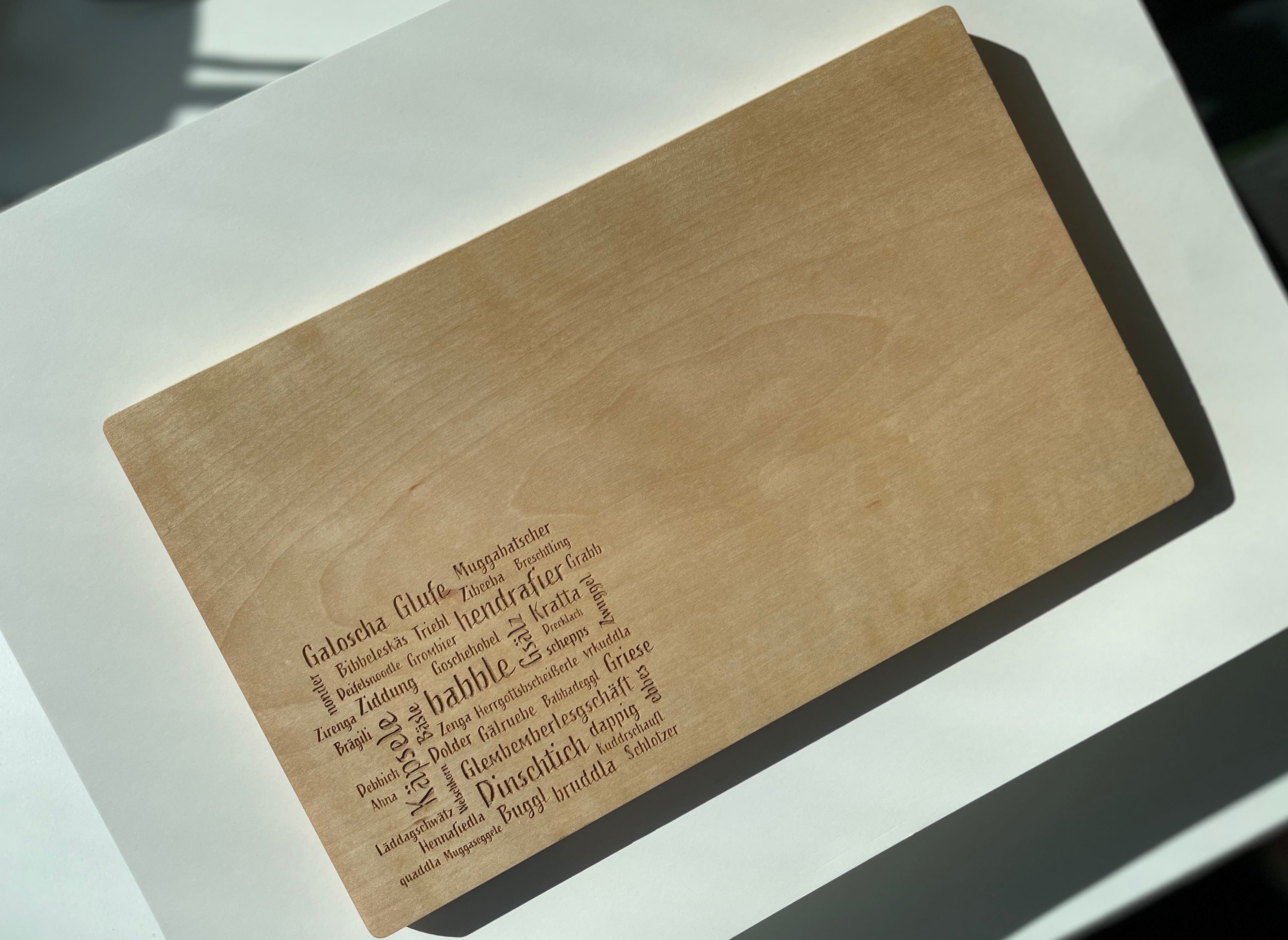 Das Mundart-Brettle ist ein hölzernes Schneidebrett, in das Wörter wie „plappern“ und „sprechen“ sowie Übersetzungen in verschiedene Sprachen eingraviert sind.