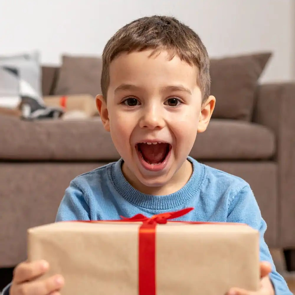 Lächelnder Junge, der ein in braunes Papier mit roter Schleife eingewickeltes Geschenk hält.