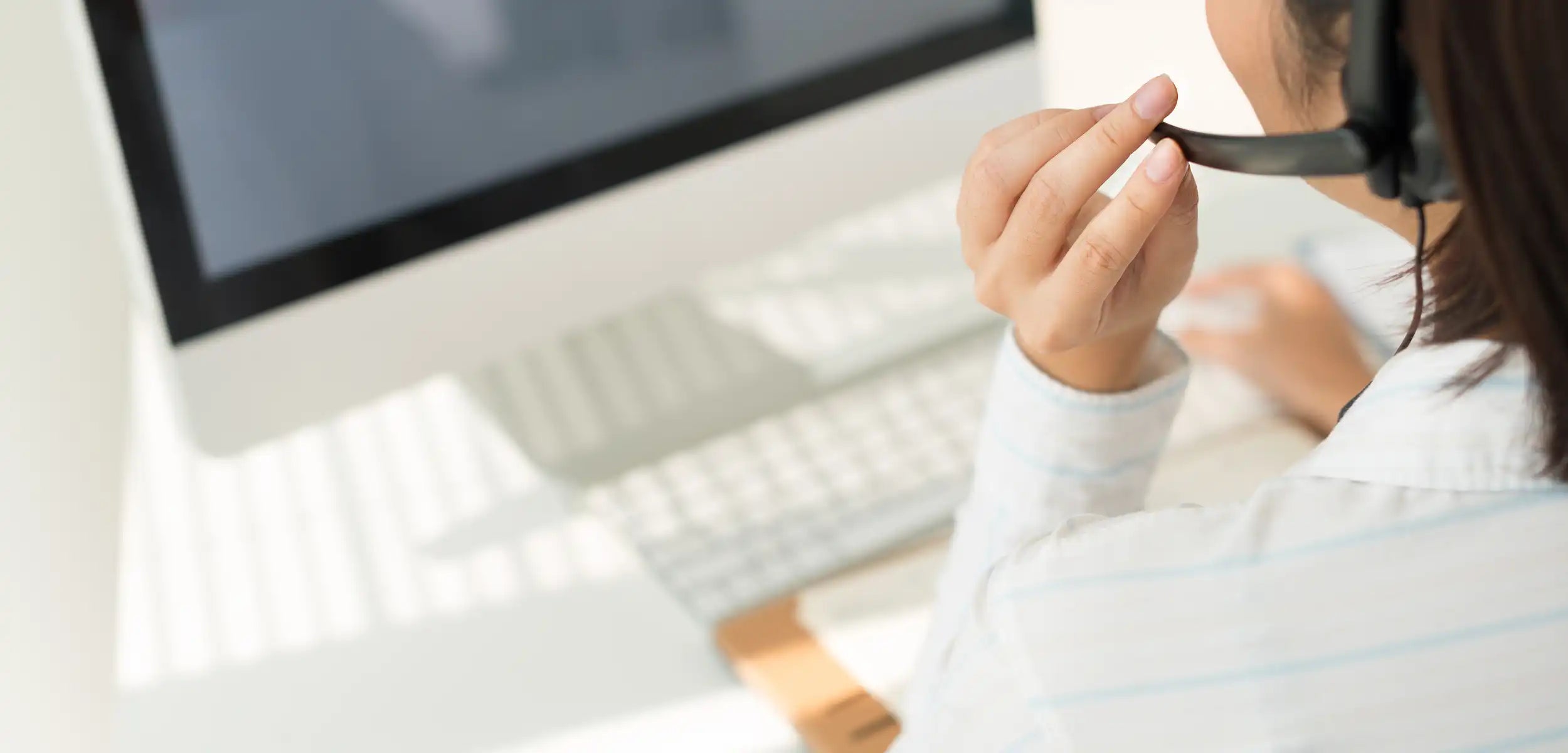 Person mit Headset bei der Arbeit an einem Computer, von hinten und leicht seitlich gesehen.