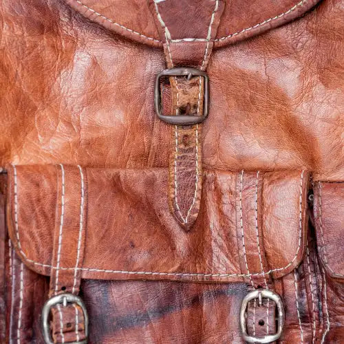 Nahaufnahme einer abgenutzten braunen Ledertasche mit Schnallen und sichtbaren Nähten.