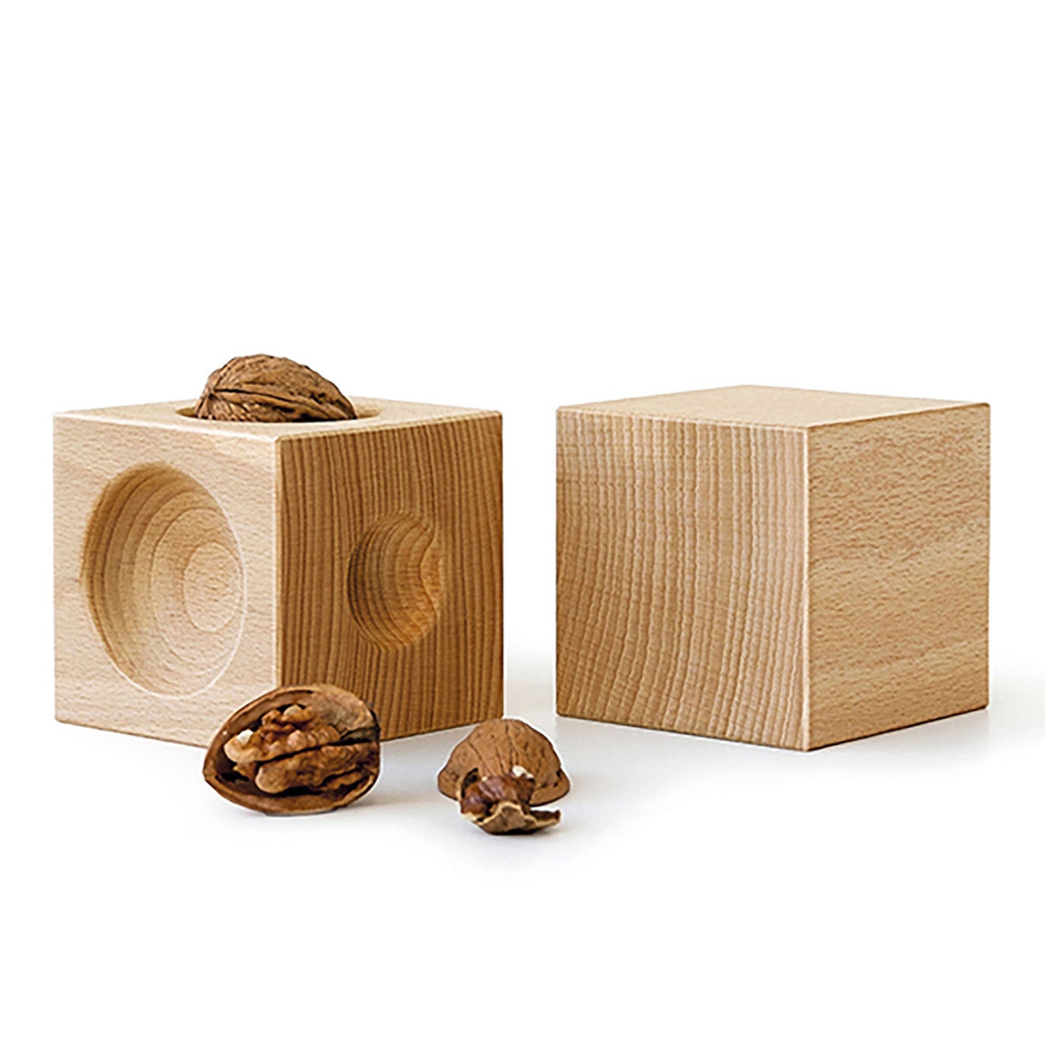 Zwei NUSSKUBUS – Nussknacker-Würfel aus Buchenholz stehen auf weißem Untergrund, einer davon mit kreisrunder Vertiefung, in der eine Walnuss sitzt. Davor gebrochene Walnussstücke betonen die Verwendung natürlicher Materialien und Nachhaltigkeit.