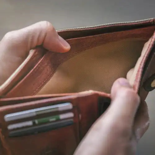 Die Hände halten eine leere braune Brieftasche mit sichtbaren Kartenfächern offen.