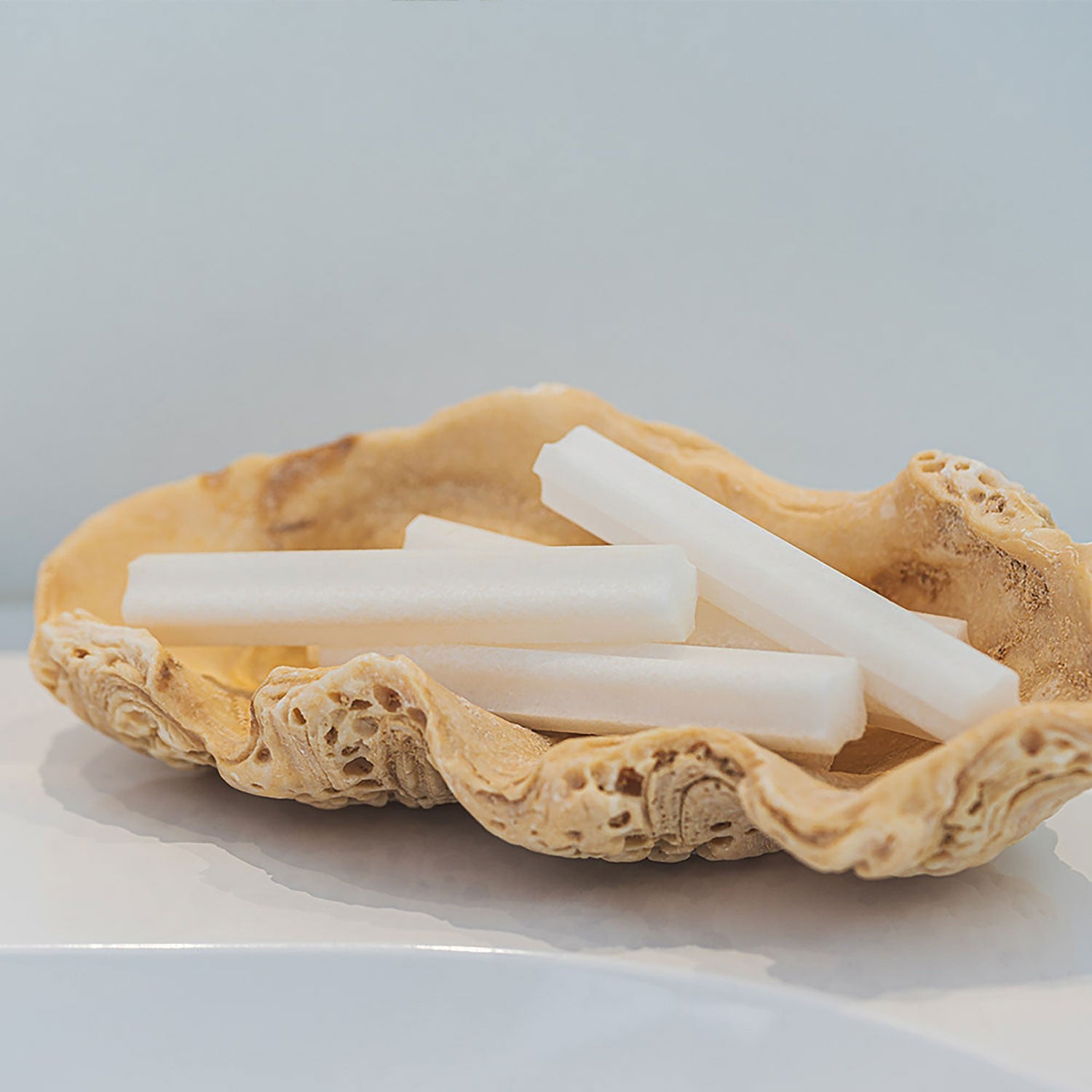 Drei weiße, zylindrische Kreidestifte ruhen elegant in einem strukturierten beigen Halter auf einer hellen Oberfläche und erinnern an die sanfte Berührung von „Deine Salzdusche für Zuhause“.