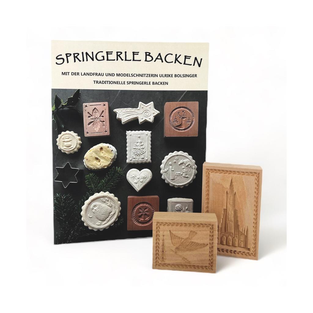 Das „Set mit 2 Holzspringerle und Buch Springerle backen“ hebt traditionelles Weihnachtsgebäck hervor, mit detaillierten Keksformen in Form von Herzen und Sternen, mit zwei markanten größeren handgeschnitzten Holzspringerle-Formen mit aufwendigen Designs.