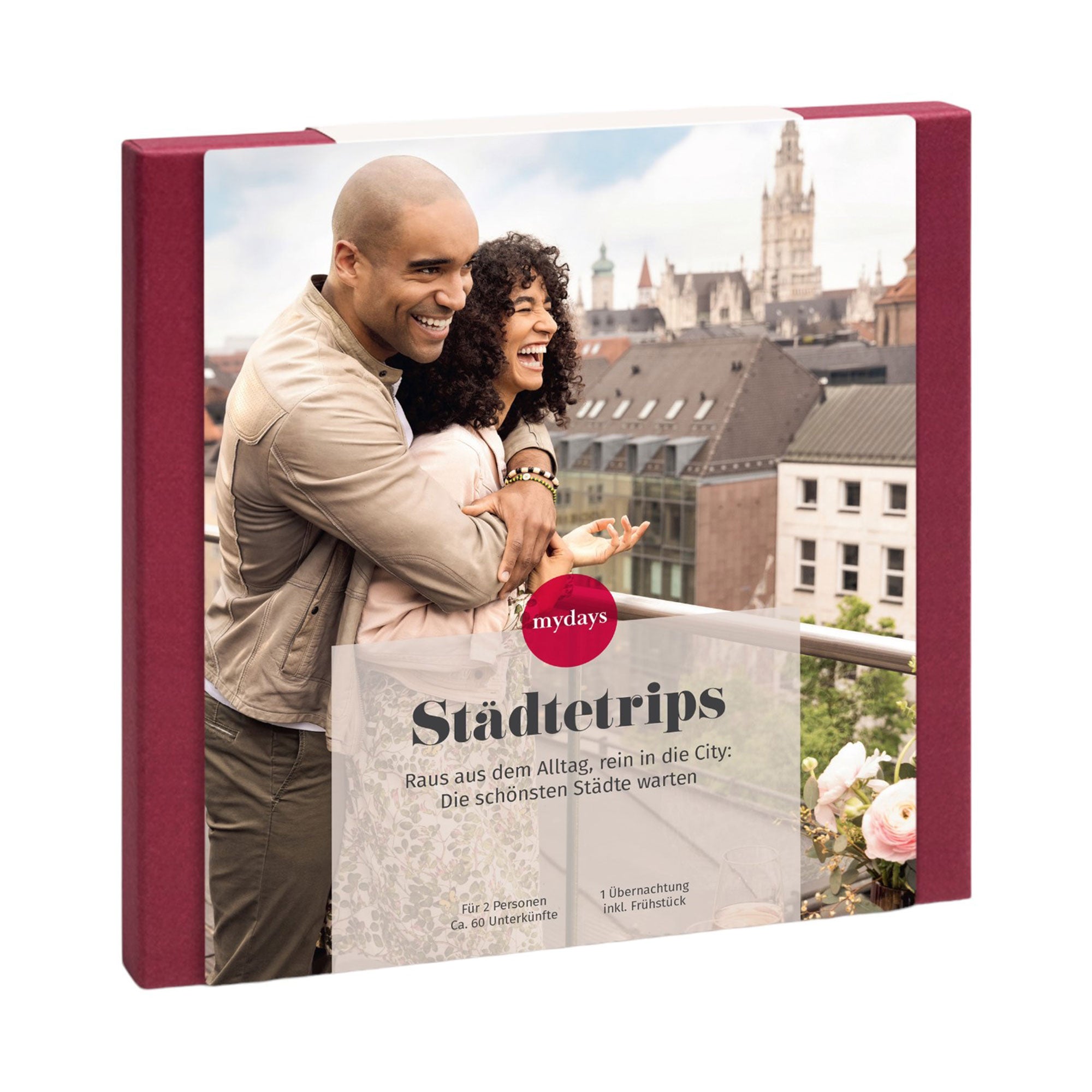 Ein lächelnder Mann und eine lächelnde Frau umarmen sich auf einem Balkon, hinter ihnen die atemberaubende Skyline einer Stadt. Dieses Bild ist Teil der „Erlebnis-Box Städtetrips“ von Mydays, die unvergessliche Städtereise-Unterkünfte für zwei Personen in Europas pulsierenden Städten bietet.