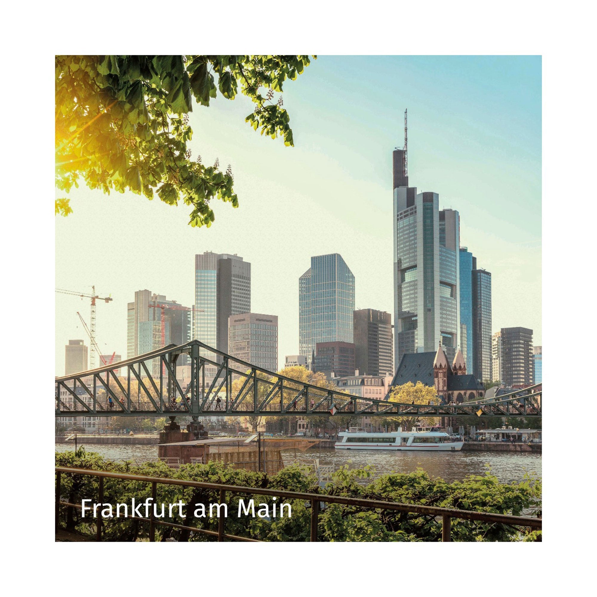 Genießen Sie mit der Erlebnis-Box Städtetrips eine malerische Fahrt durch die Skyline von Frankfurt am Main, wo moderne Wolkenkratzer und historische Bauwerke am Fluss aufeinandertreffen. Eine Brücke spannt sich elegant über das Wasser, während ein Boot vorbeigleitet, und Bäume rahmen diese urbane Szene unter klarem Himmel ein.