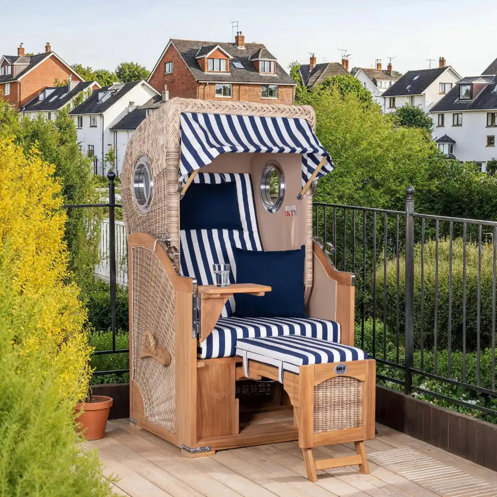 Ein blau-weiß gestreifter Strandkorb auf einer Terrasse, dahinter Häuser.