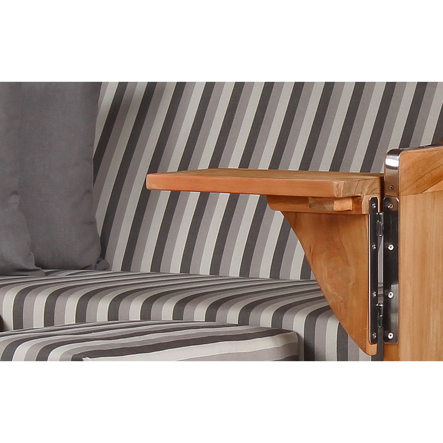 Eine Nahaufnahme zeigt einen klappbaren Teakholztisch, der am Strandkorb DÜNE befestigt ist. Die Sitzfläche ist grau gestreift und mit grau-weißen Streifen versehen. Der Tisch ist umgeklappt, wodurch die grauen Kissen im Hintergrund hervorgehoben werden.