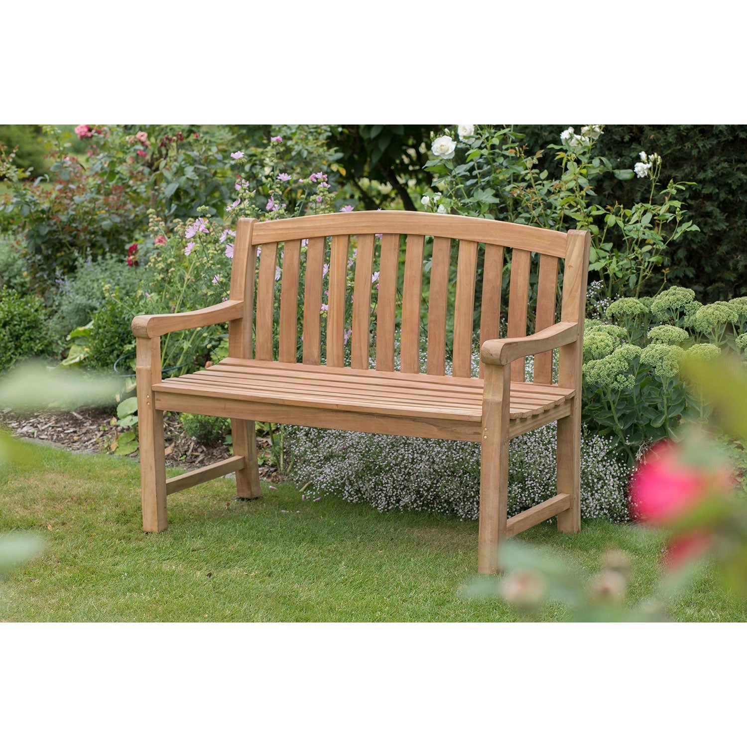 Die Gartenbank aus Holz 2-Sitzer steht auf einer grünen Wiese, umgeben von Pflanzen und Blumen – perfekt für eine stilvolle Gartengestaltung im Freien.