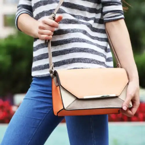 Frau in gestreiftem Hemd und Jeans mit einer farbigen Crossbody-Tasche im Freien.