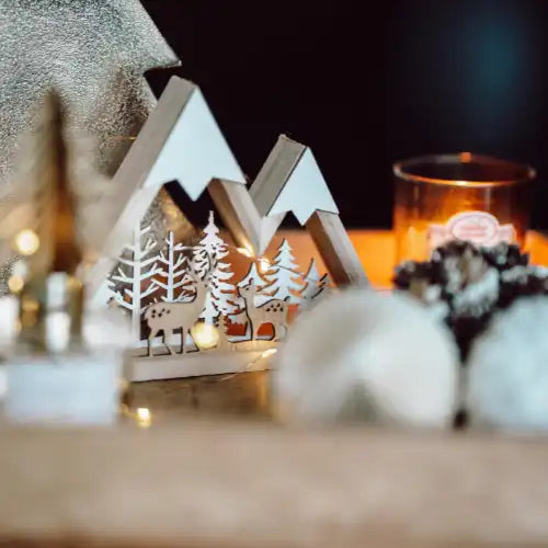 Winterszene aus Holz mit Rehen, Bäumen, Lichterketten, Kerzen und Tannenzapfen.