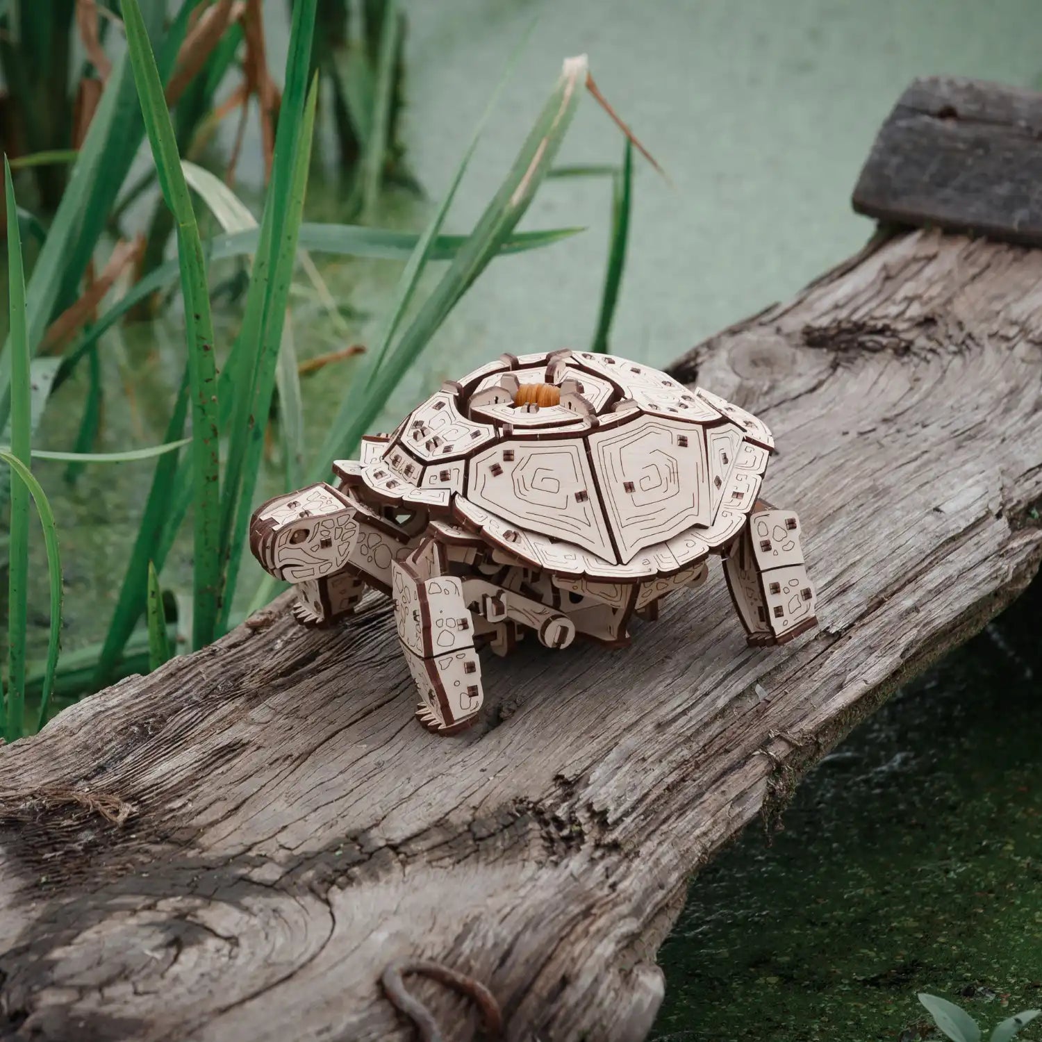 Das 3D-Holzpuzzle „Mechanische Schildkröte“ steht auf einem Baumstamm inmitten von üppigem Gras und Wasser. Sein detailreicher Panzer mit Zahnrädern und mechanischen Elementen verleiht ihm einen Steampunk-Look und verstärkt seinen bezaubernden Charme.
