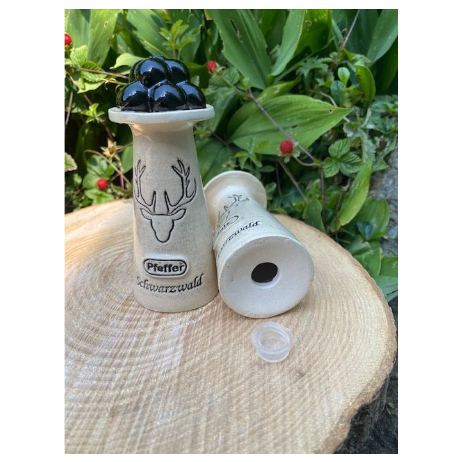 Zwei handgefertigte Streuer aus dem Schwarzwald Salz- und Pfefferstreuer Set „Wendelin“: Einer steht gefüllt mit schwarzen Pfefferkörnern aufrecht, der andere liegt dekorativ daneben.