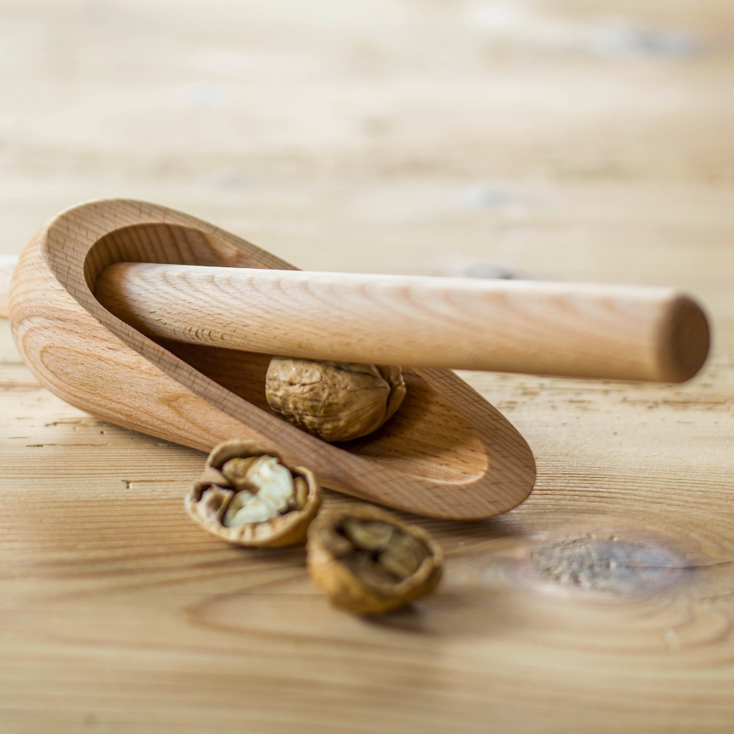 Der Nussknacker Nuss Besteck mit einer Walnuss darin und geknackten Walnussstücken auf einer Holzoberfläche – ein nachhaltiges Geschenk für Genießer.