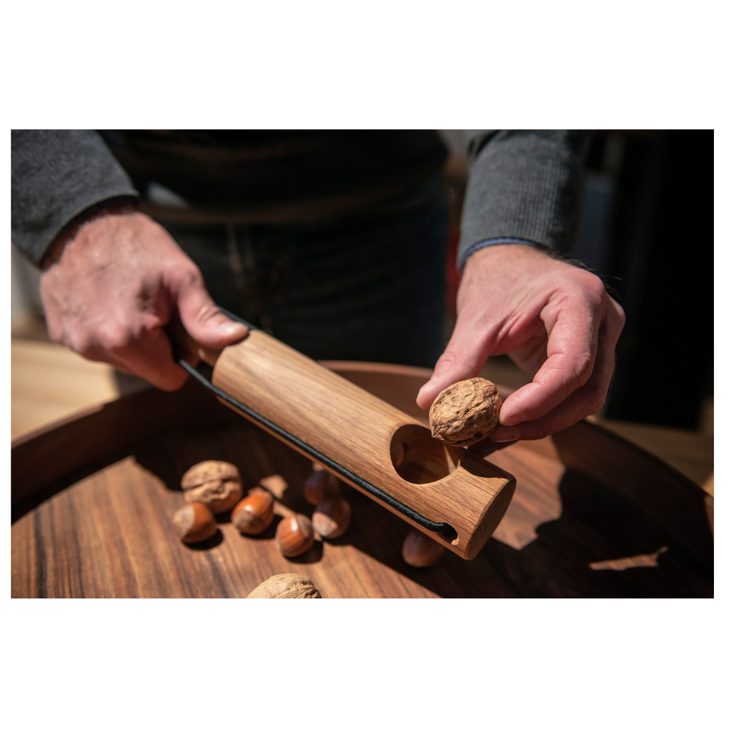 Hände knacken mit dem Nussknacker Nuss Kracher eine Walnuss über einer Holzschale mit verschiedenen Nüssen, gefertigt aus edlem Eichenholz im Stil von Dietmar Mechsner.
