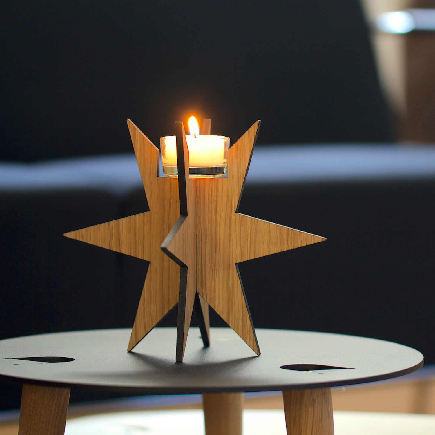 Eine brennende Kerze in einem Teelichthalter Sternenlicht steht auf einem kleinen runden Tisch und bringt gemütliche Weihnachtstradition in den modernen Raum.