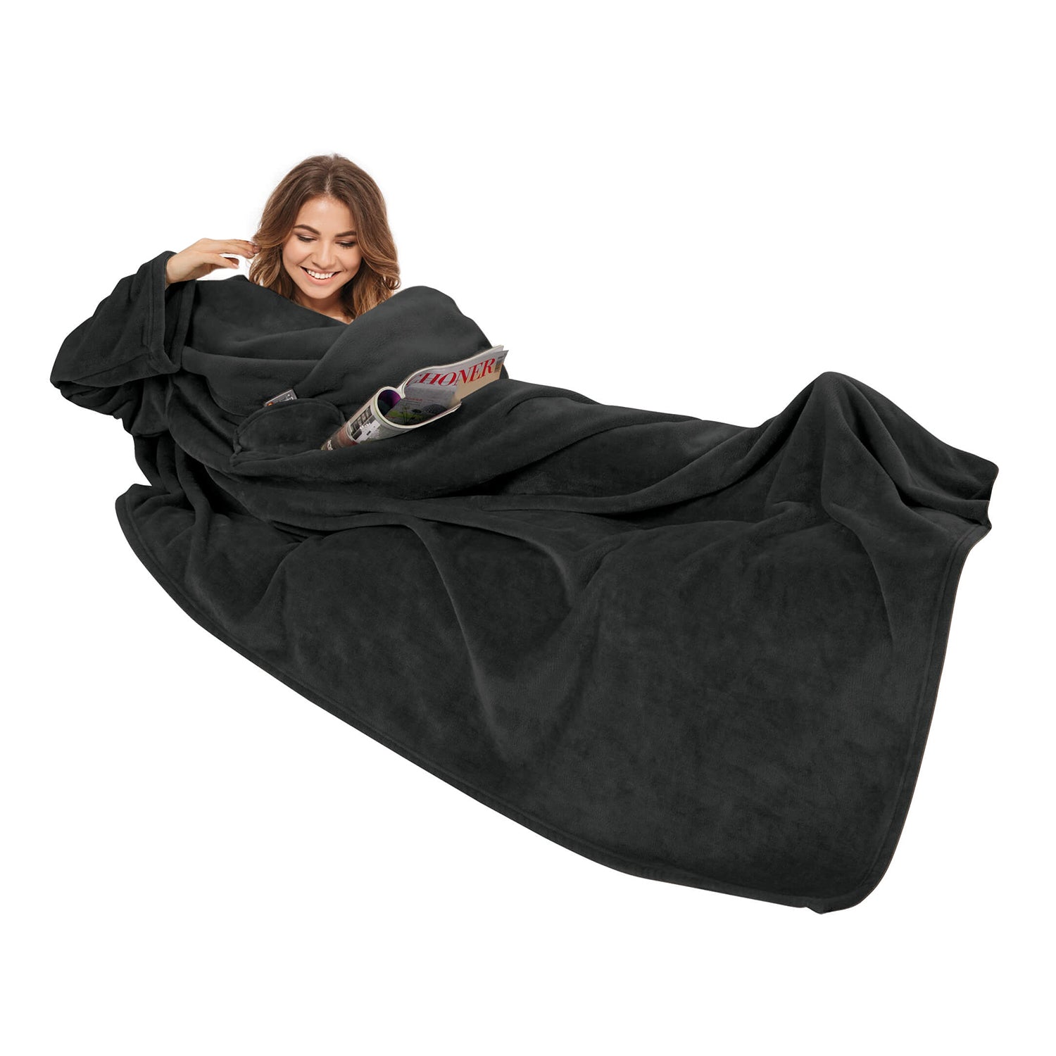 Frau lächelt in einer Kuscheldecke mit Ärmeln 150x240 cm und liest eine Zeitschrift.