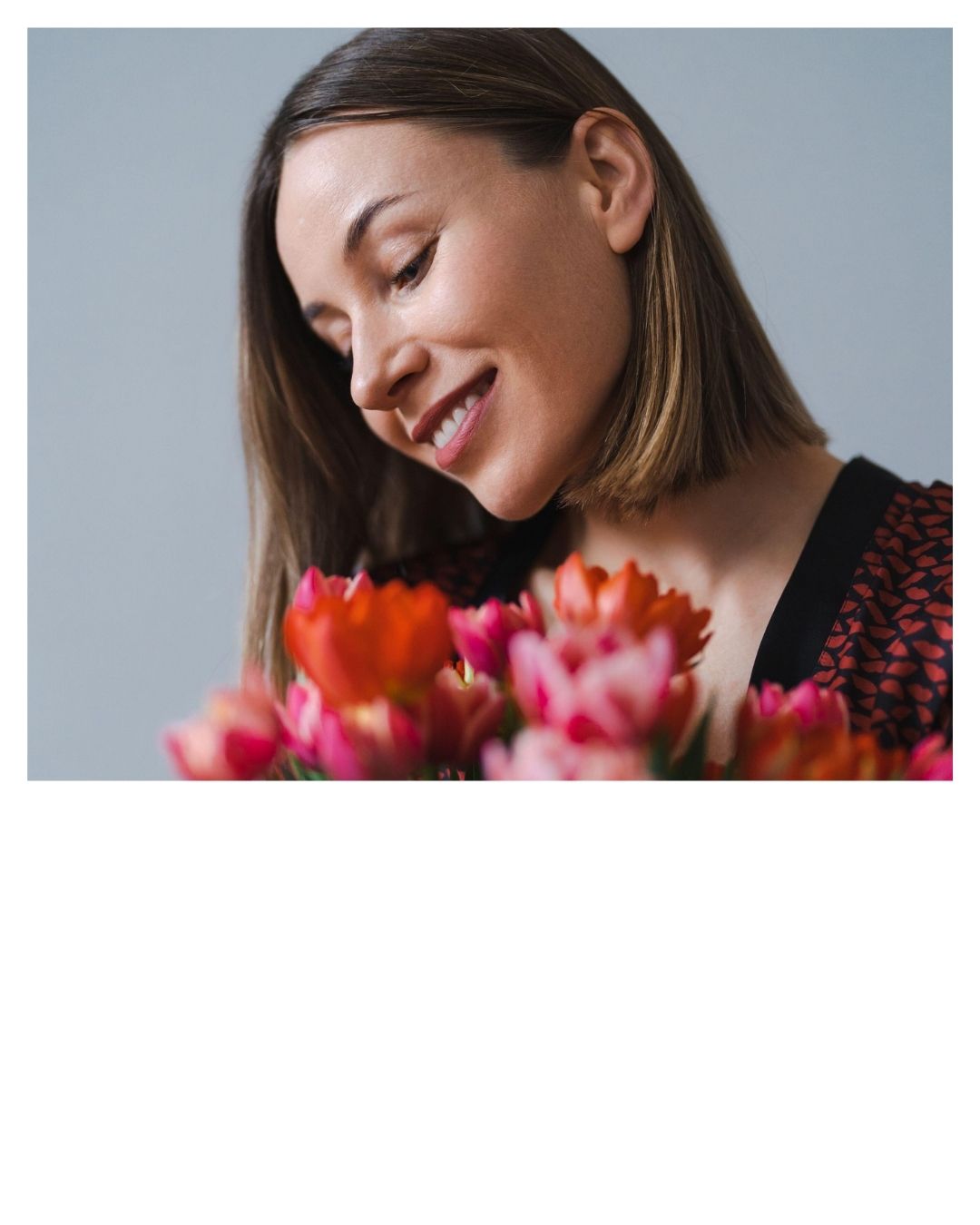 Frau lächelt und hält einen Strauß mit rosa und roten Blumen.