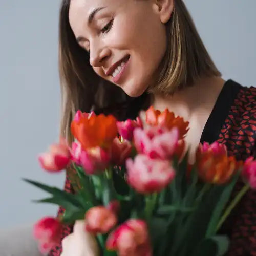 Frau lächelt, während sie einen Strauß rosa und orangefarbener Tulpen hält.