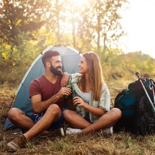 Ein Pärchen sitzt in einem Zelt im Freien, lächelt und hält Getränke in der Hand.