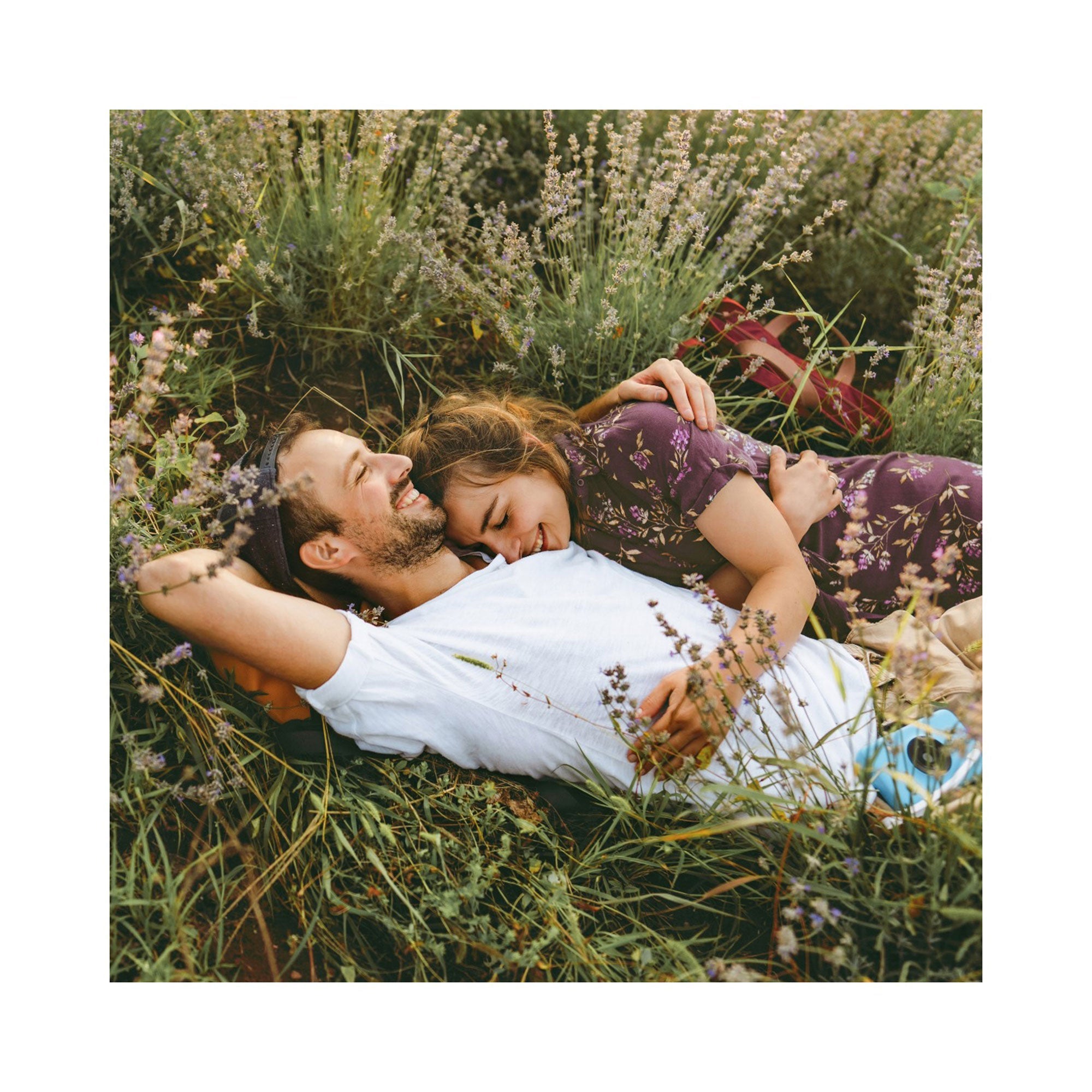 Ein Paar erlebt die „Erlebnis-Box 3 Tage Du & Ich“ auf einer Wiese mit Wildblumen. Die Frau im geblümten Kleid lehnt lächelnd an der Schulter des Mannes. Er entspannt sich in seinem weißen Hemd, die Hände hinter dem Kopf verschränkt. Ihr Ausflug entfaltet sich wie das Öffnen eines besonderen Geschenks gemeinsamer Momente.