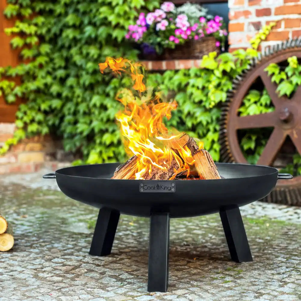 Eine lodernde Feuerstelle mit brennenden Holzscheiten auf einer Gartenterrasse.