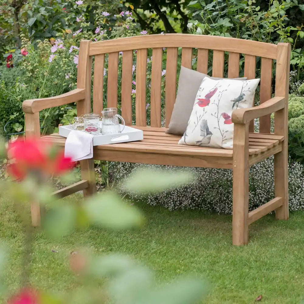 Gartenbank aus Holz mit zwei Kissen und einem Tablett für Getränke und Gläser.