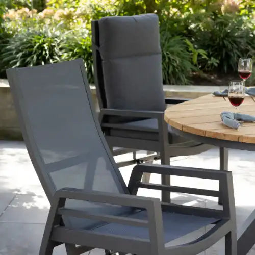 Zwei Terrassenstühle und ein runder Tisch mit Weingläsern im Freien.