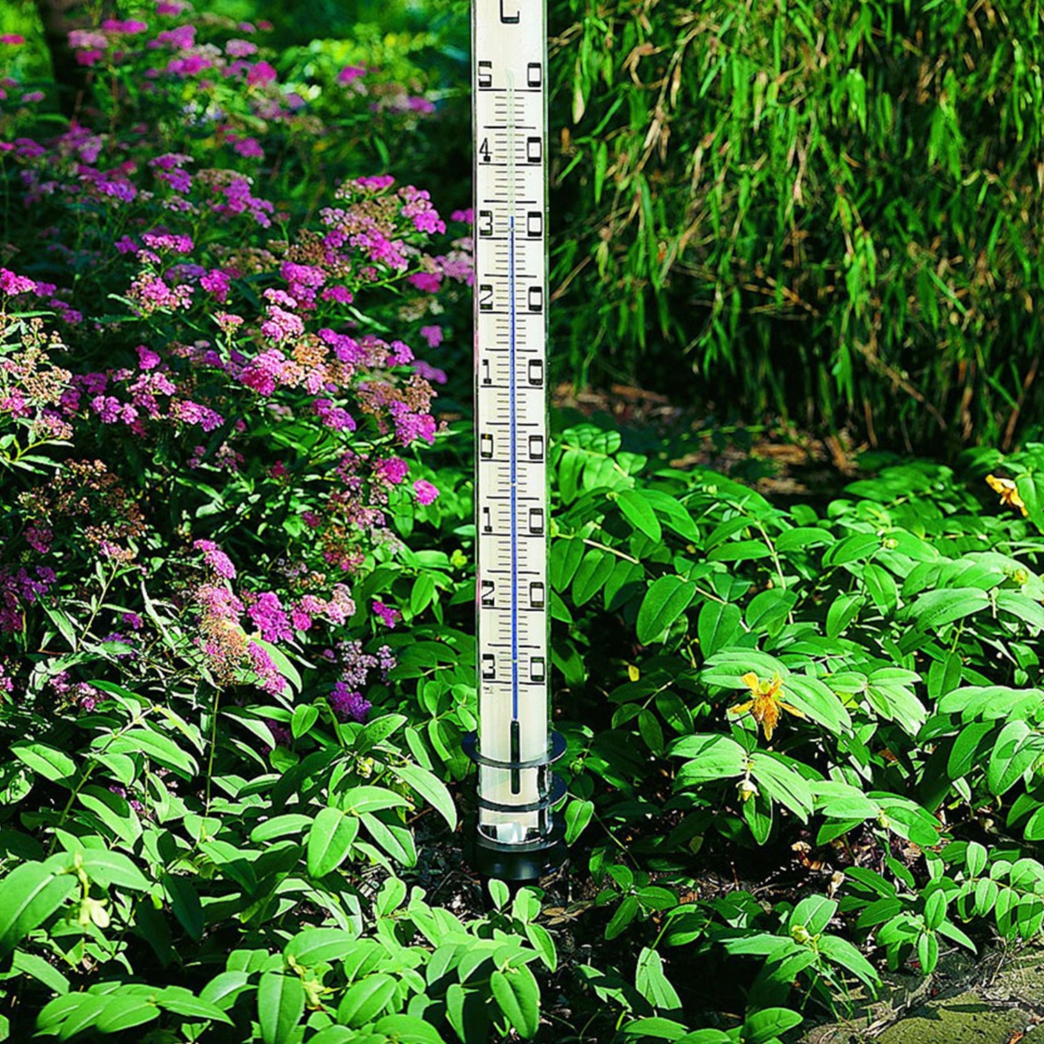 Ein Großes Gartenthermometer steht neben Blumen im grünen Garten.