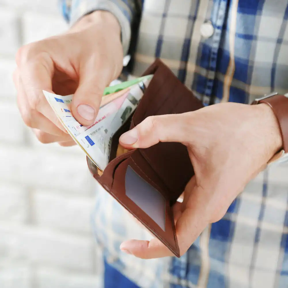 Person mit offener Brieftasche mit Bargeld und Karten, die ein kariertes Hemd trägt.