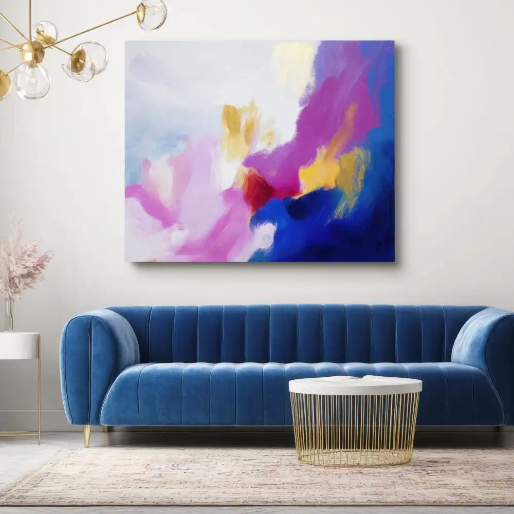 Abstraktes buntes Gemälde über einem blauen Samtsofa und einem runden weiß-goldenen Couchtisch.