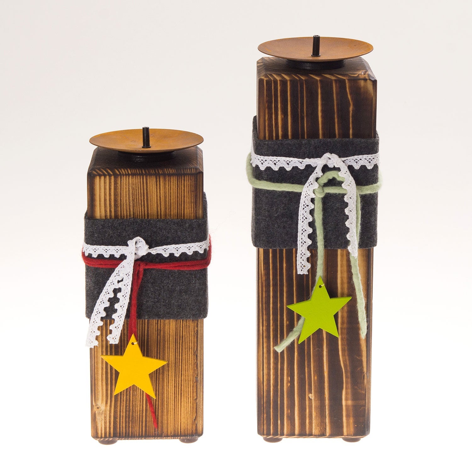 Zwei Kerzenständer aus Holz mit gebrannter Oberfläche stehen nebeneinander, umwickelt mit Filz- und Spitzenbändern und geschmückt mit gelben Sternanhängern. Der größere Kerzenständer rechts, „Kerzenständer aus Holz – groß“, wartet sehnsüchtig auf Stumpenkerzen auf seiner Metallplatte.