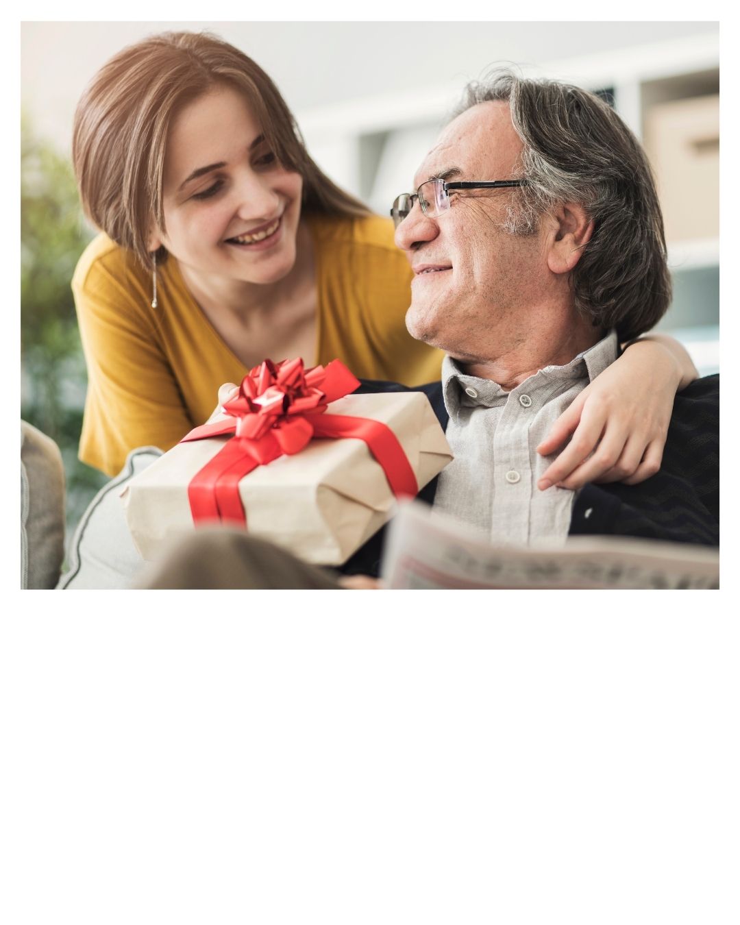 Eine Frau überreicht einem älteren Mann ein Geschenk mit einer roten Schleife, beide lächeln herzlich.