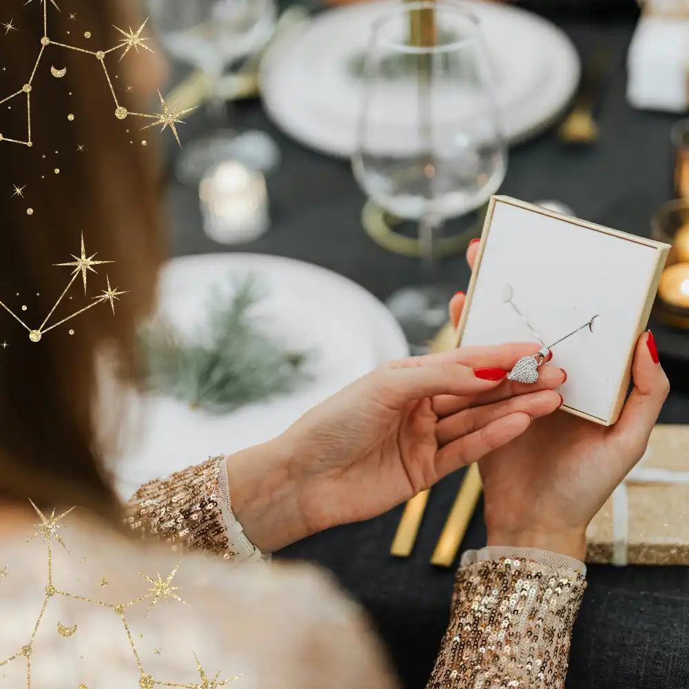 Frau hält eine herzförmige Halskette in einer Schachtel an einem festlichen Tisch.