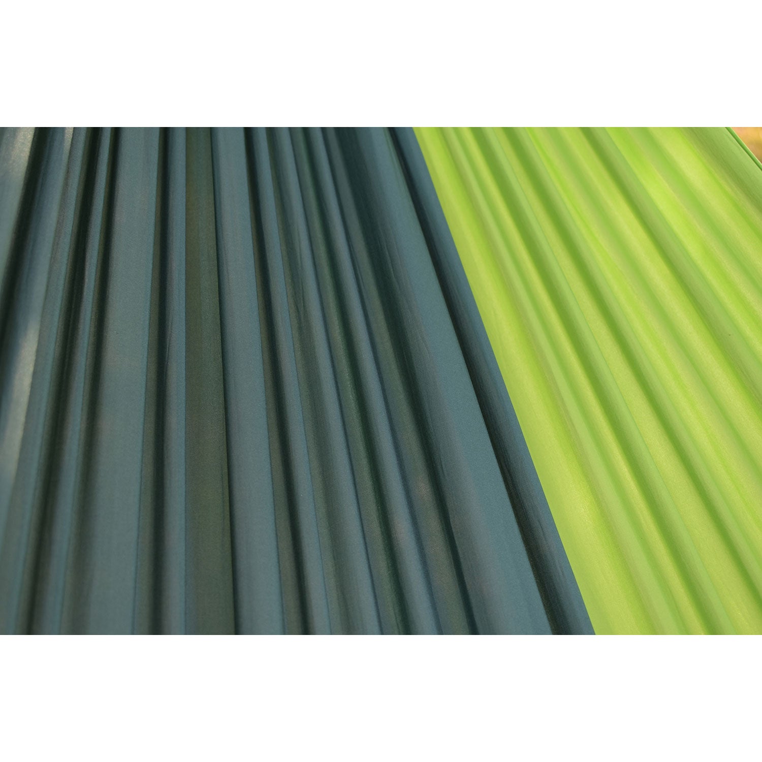 Eine Nahaufnahme zeigt zwei superleichte Hängematten für den Außenbereich in Dunkelgrün und Limettengrün. Der robuste Stoff ist zu einem Streifenmuster gefaltet. Sonnenlicht hebt die Texturen und Farben des Materials hervor und wirft weiche Schatten.