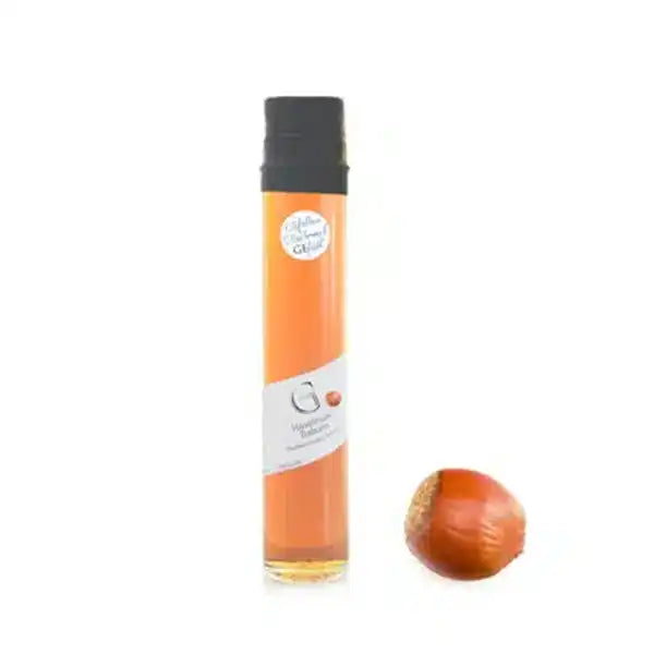 Ein Fläschchen mit Haselnusslikör neben einer ganzen Haselnuss auf weißem Hintergrund.