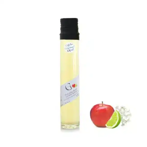 Hohe Flasche mit gelber Flüssigkeit, daneben ein Apfel, eine Limettenscheibe und weiße Blumen.